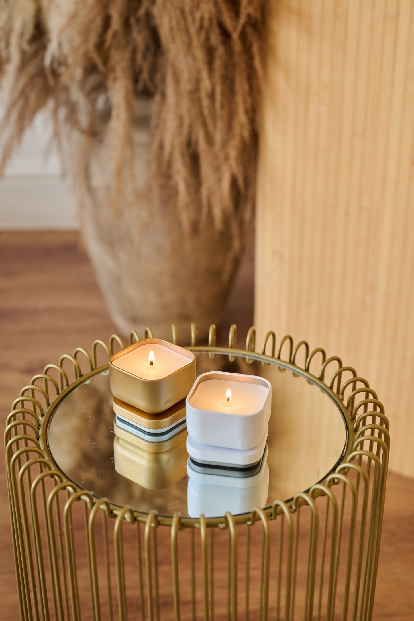 Two candles on a small round table with a decorative plant in the background