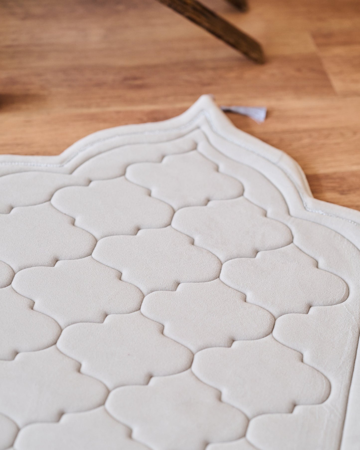 textured memory foam prayer mat on a wooden floor with a modern sofa and decor in the background.