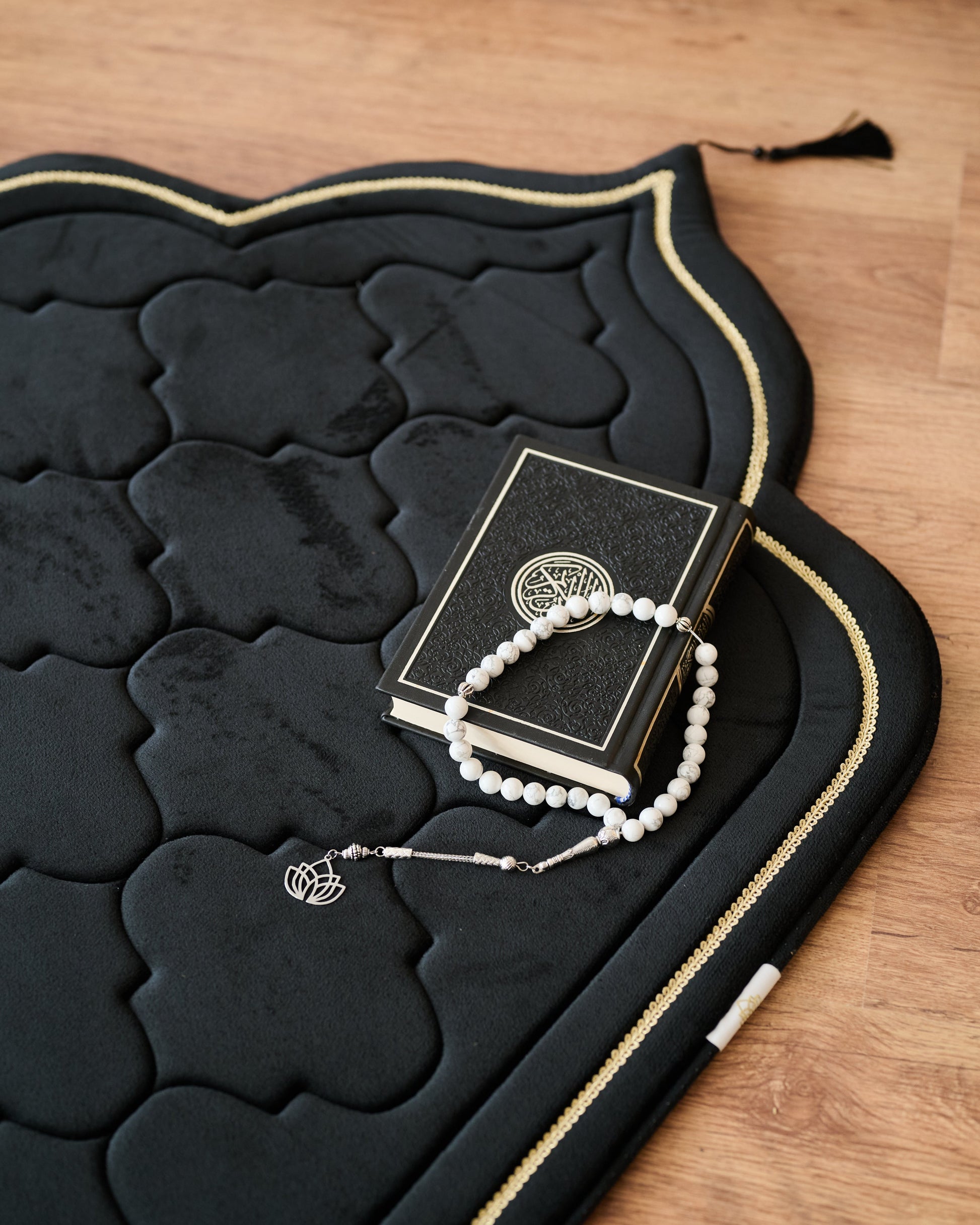 Black prayer mat with a book and rosary on a wooden surface