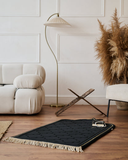 Black rug with tassels on a wooden floor in a living room setting.