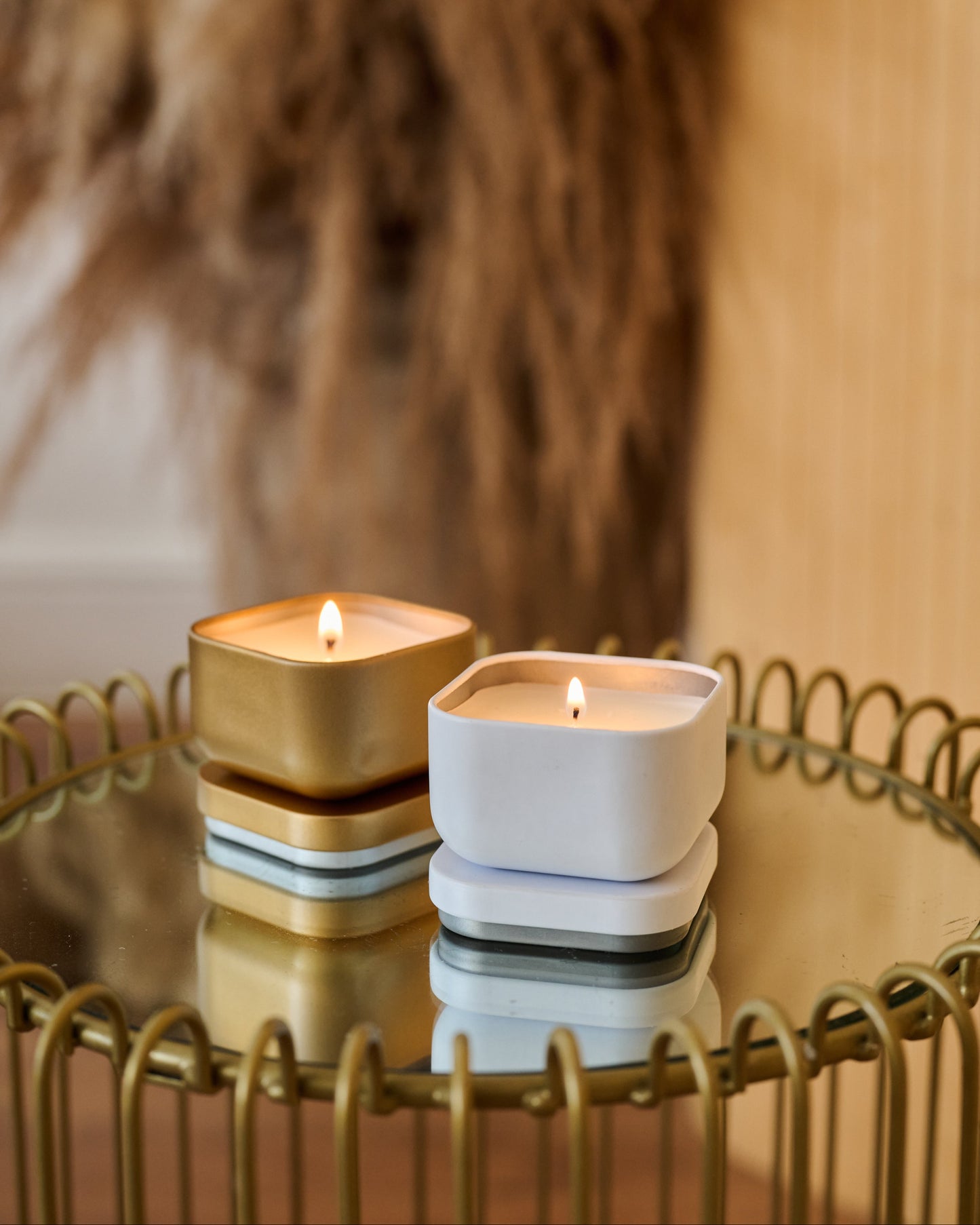 Two candles, one gold and one white, on a reflective surface with a blurred background.