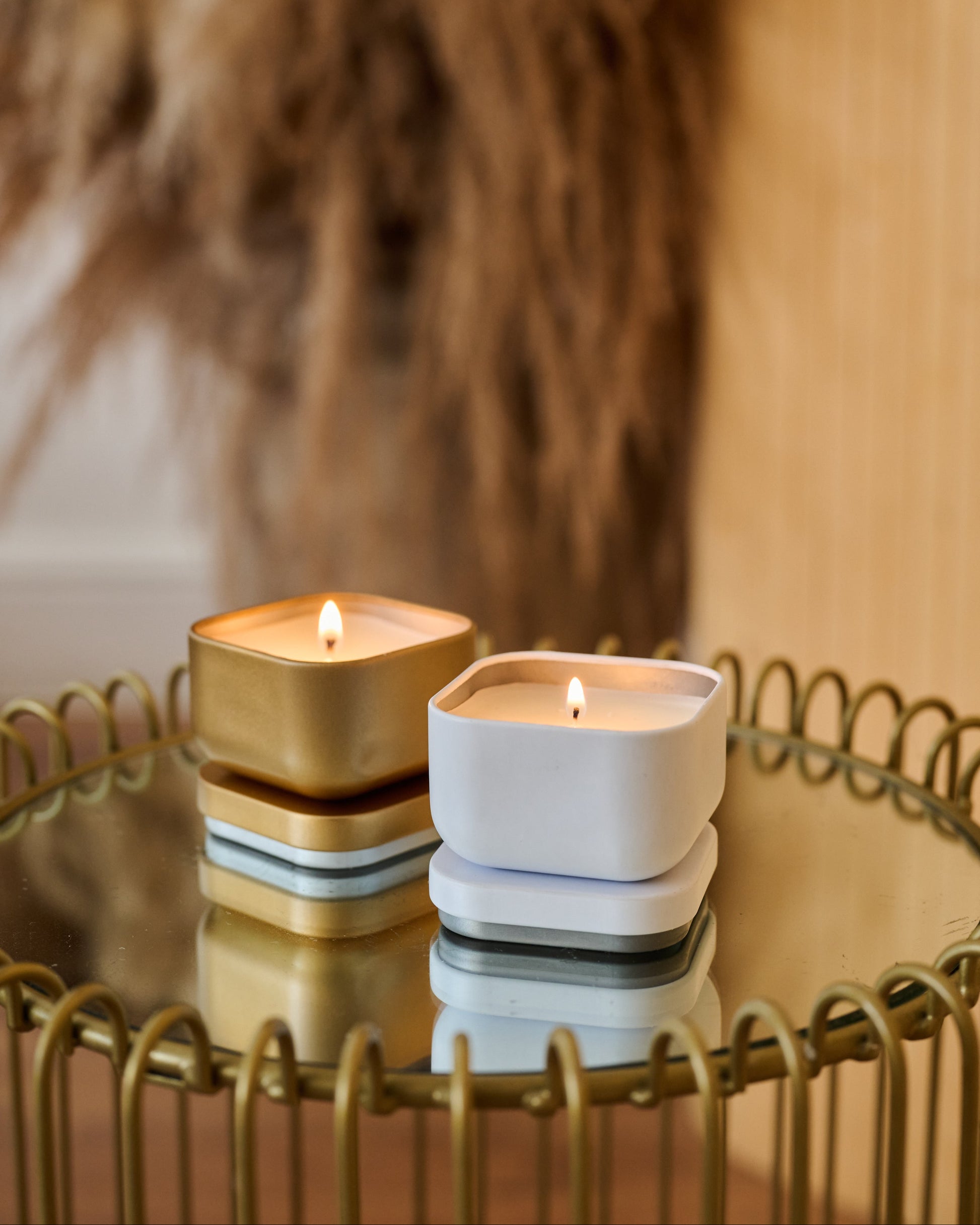 Two candles, one gold and one white, on a reflective surface with a blurred background.
