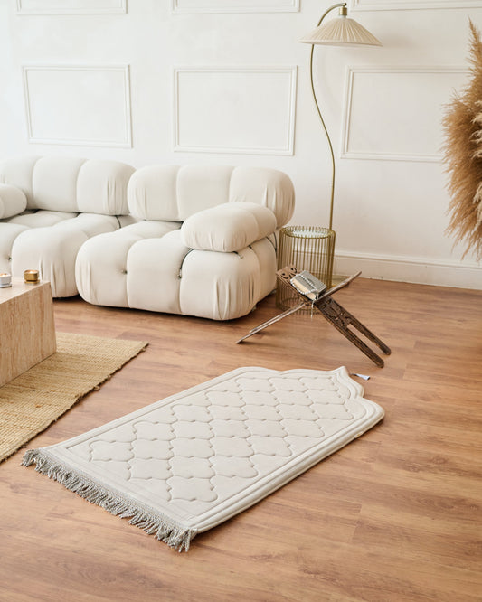 textured memory foam prayer mat on a wooden floor with a modern sofa and decor in the background.