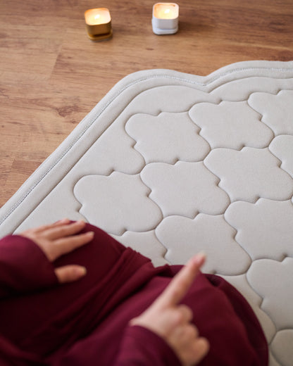 textured memory foam prayer mat on a wooden floor with a modern sofa and decor in the background.