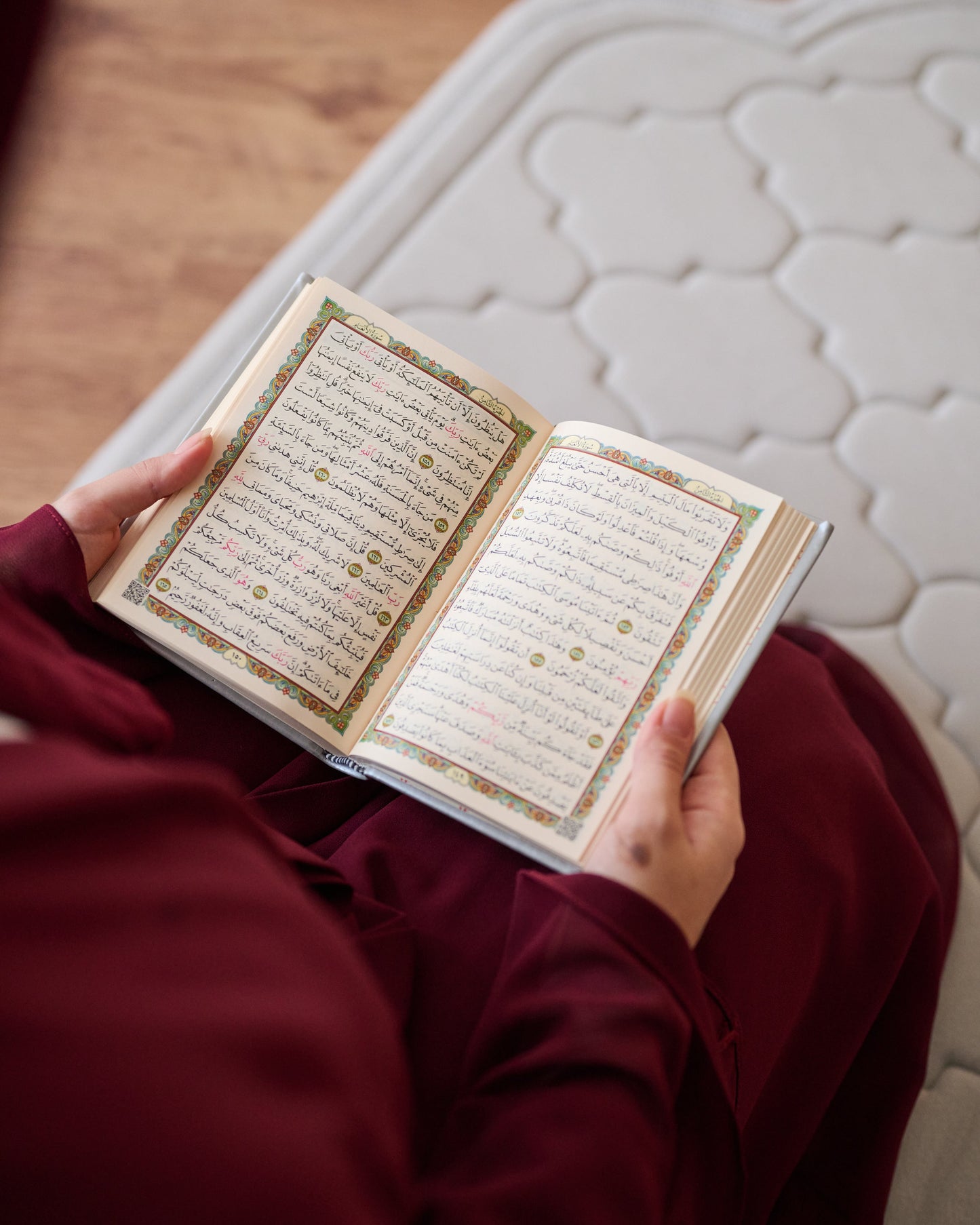 Person holding an open book with text, sitting on a mattress.