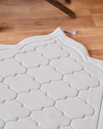 textured memory foam prayer mat on a wooden floor with a modern sofa and decor in the background.