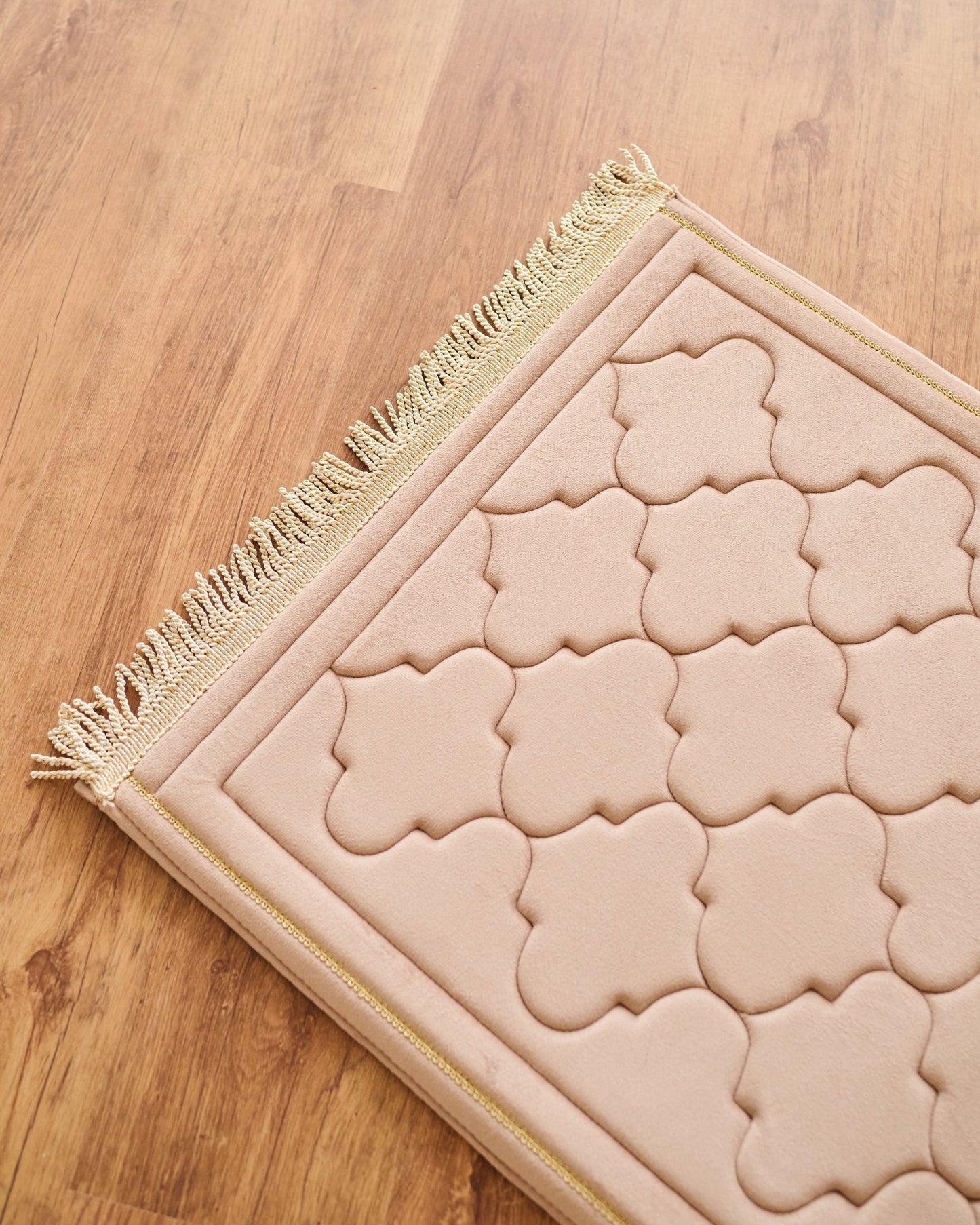 Beige prayer mat with intricate patterns on a wooden floor