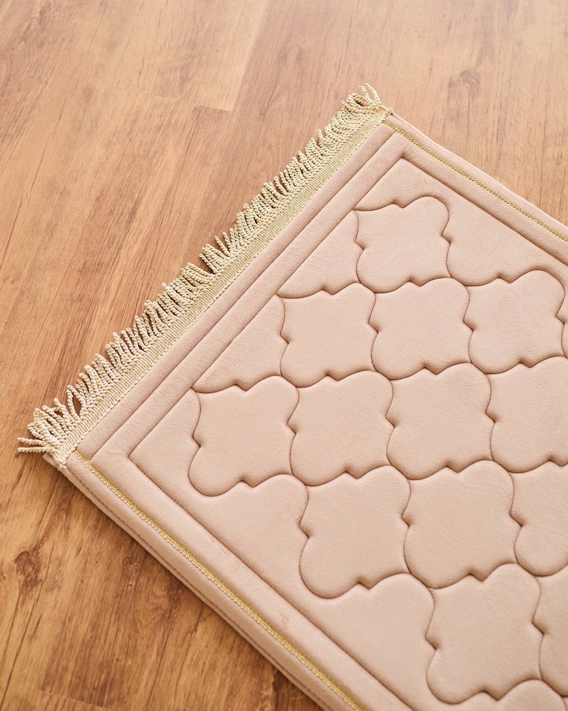Beige prayer mat with intricate patterns on a wooden floor