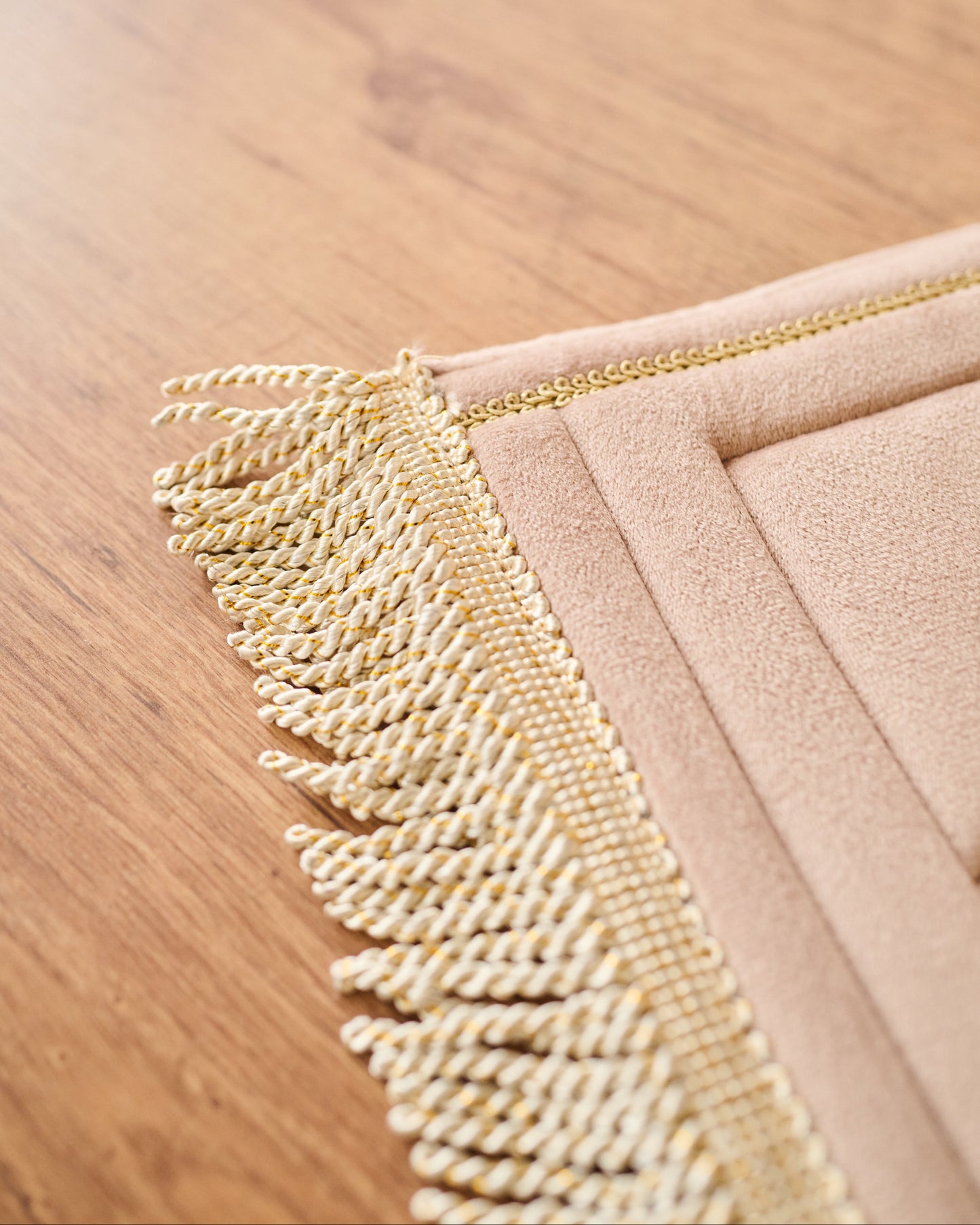 Close-up of a textured gold fringe on a beige fabric against a wooden surface